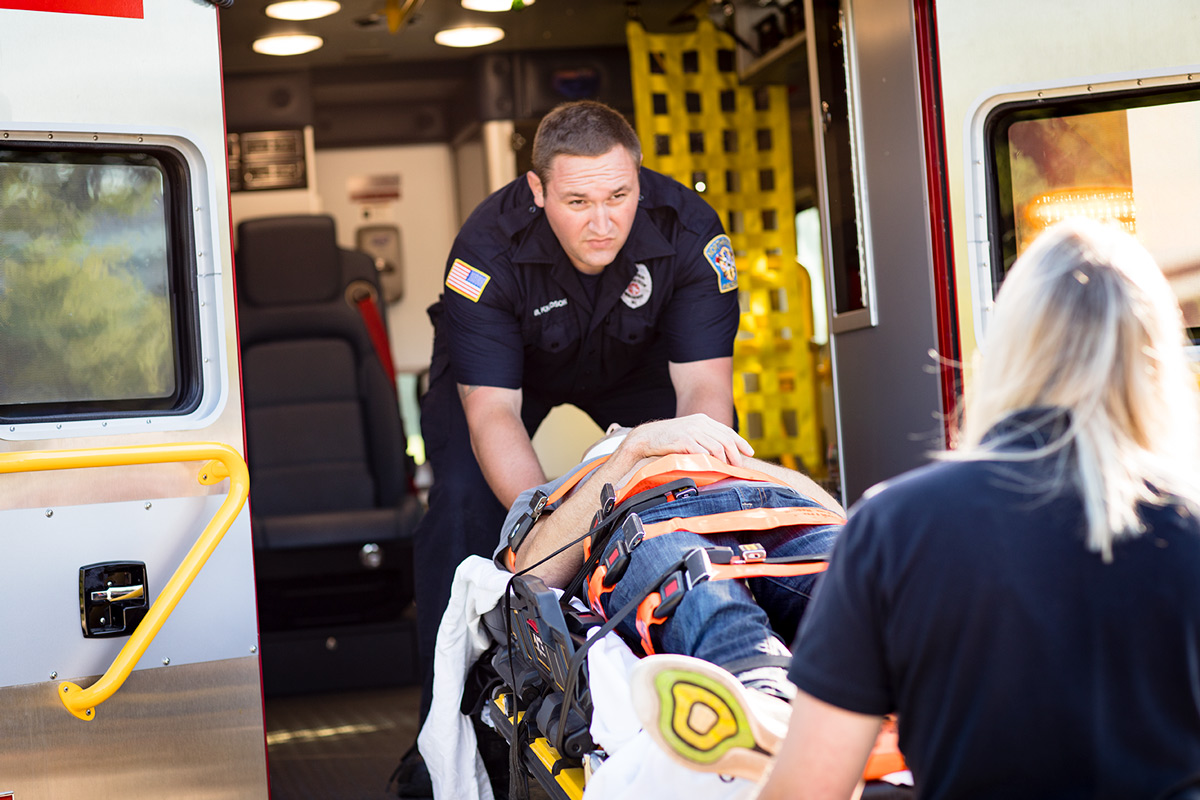 emt Two emergency medical technicians lifting man on stretcher into ambulance.