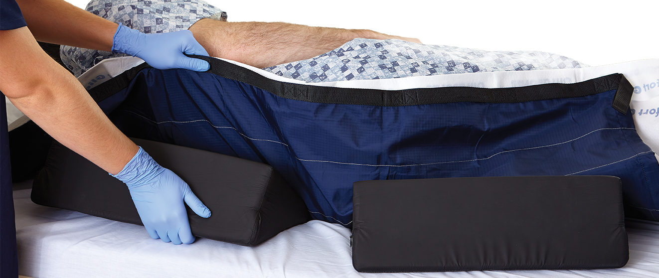 Nurse positioning wedges under a patient lying in a bed. Nurse positioning wedges under a patient lying in a bed.