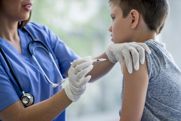 Nurse in blue scrubs and gloves administering a shot to a child
