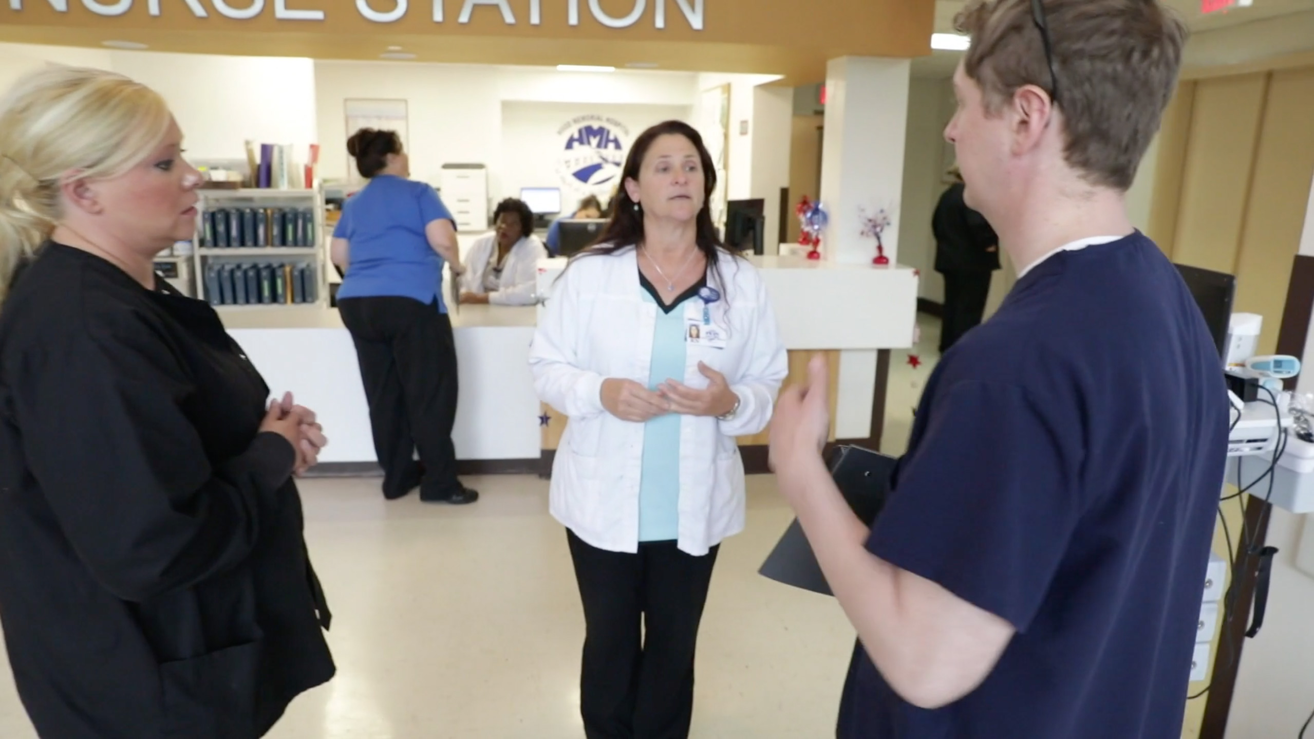 Two female and one male hospital employees in a small group discussion at a nurses station