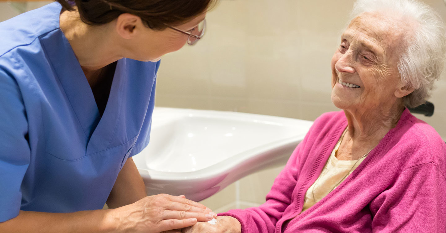 A nurse applies moisturizer to the hand of an elderly woman in a wheelchair. A nurse applies moisturizer to the hand of an elderly woman in a wheelchair.
