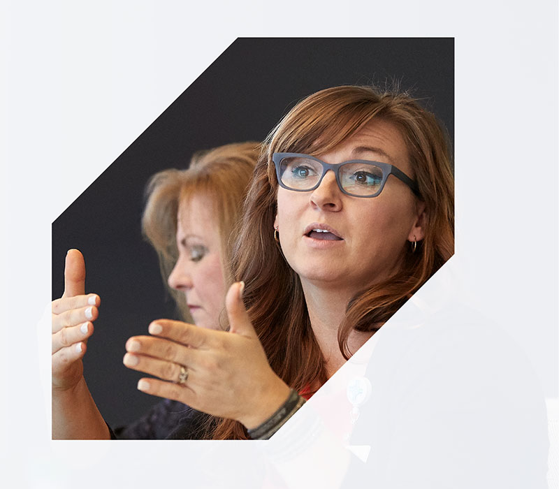 leadership Picture of two women one wearing glasses speaking with hands raised in emphasis. Photo partially covered by a graphic