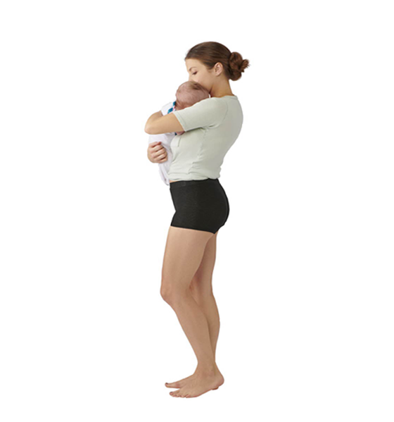 Side view of a woman holding a baby wearing a green short sleeve top and short black fitted shorts