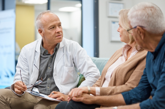 Doctor in white coat consulting with a male and female patient who are holding hands