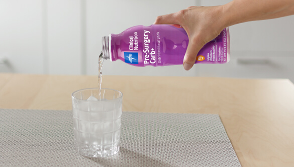 Hand pouring a bottle of Pre-Surgery Carb+ into a glass of ice, sitting on a table Hand pouring a bottle of Pre-Surgery Carb+ into a glass of ice, sitting on a table