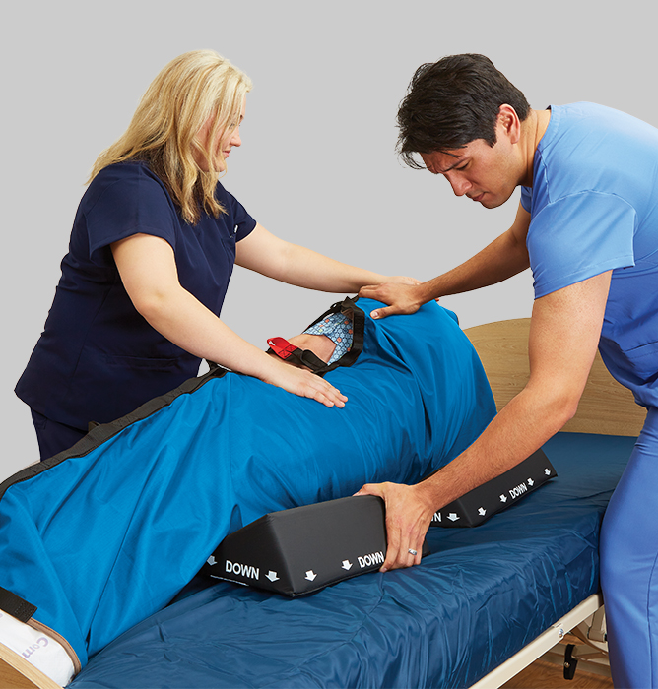 Repositioning in ICU hero image 1 Two healthcare workers in scrubs using wedges to reposition a patient