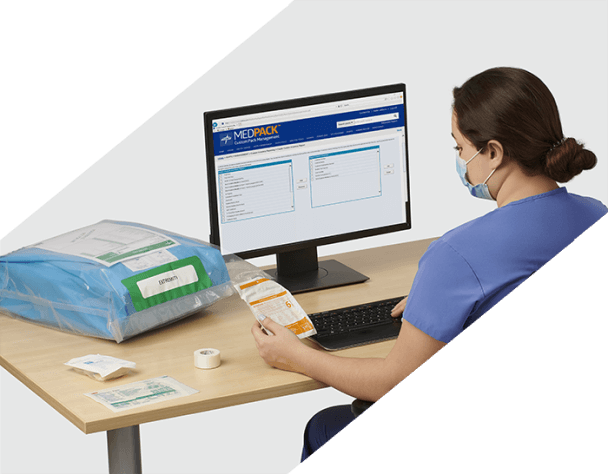 A person in scrubs and a mask at a desk entering infomration from a surgical pack into a computer.