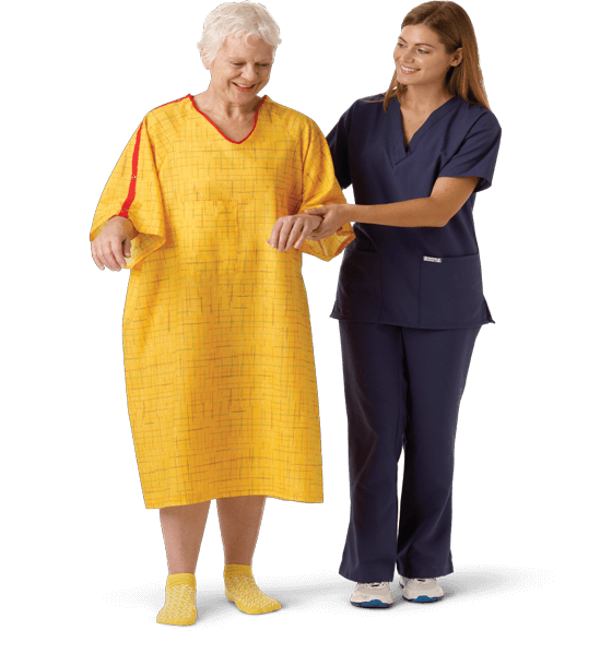 Elderly woman in bright yellow patient gown receiving walking assistance by caregiver in navy scrubs 