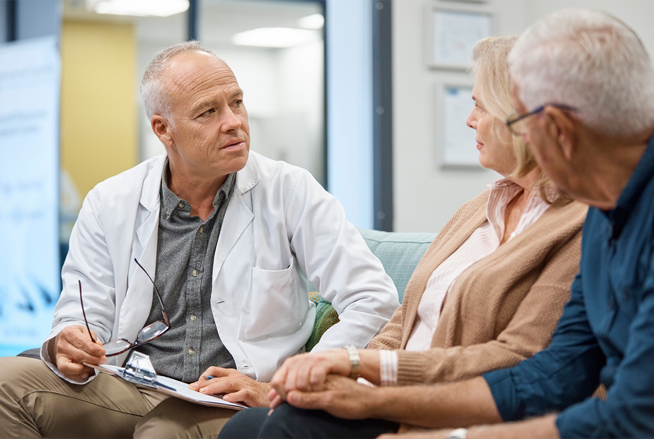 Doctor in white coat consulting with a male and female patient who are holding hands