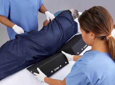 Caregivers moving patient with repositioning sheet, while sliding ComfortGlide wedges under them