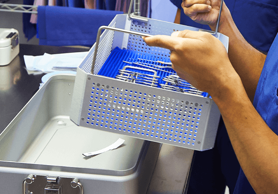 STK_Central Sterile process SPD worker holding a basket of surgical instruments, ready to set it in a sterilization container