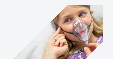 Arrow-shaped close-up of caregiver hands adjusting an OxyMask™, oxygen mask on a young girl