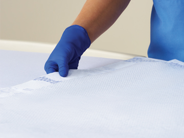 Image 2 (Optional) Gloved caregiver laying an Ultrasorbs on a bed