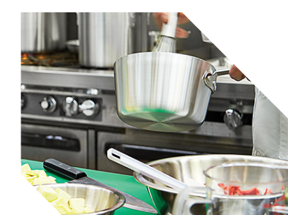 Chef whisking a pot of food above a kitchen counter with mixing bowls and utensils; a commercial stove in the background