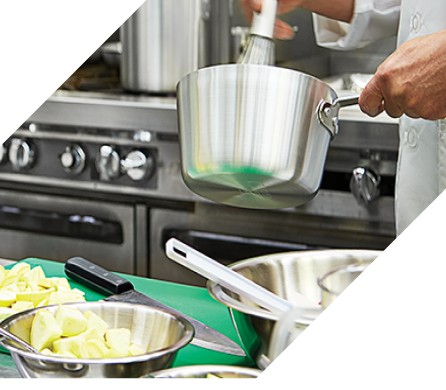 Chef whisking a pot of food above a kitchen counter with mixing bowls and utensils; a commercial stove in the background