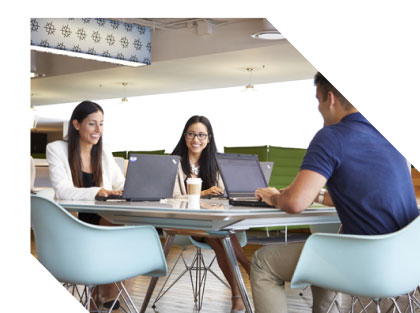 Two women and a man meeting at a conference table with open laptops