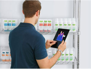 Man in a hospital supply room comparing inventory data on a tablet with shelf stock 