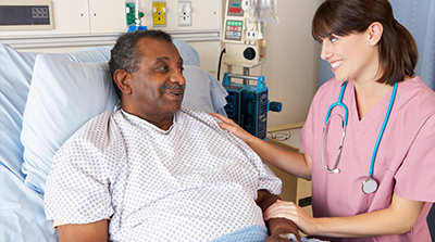 Nurse standing at bedside of older male patient in hospital