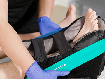 Caregiver’s gloved hands adjusting patient’s heel offloading boot