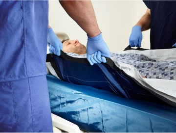 Patient being moved by two caregivers using a patient repositioning system
