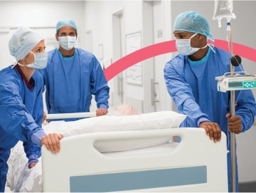 Three caregivers push a patient in a hospital bed