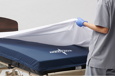 Gloved caregiver hands dispense ISP protectant cream to elderly patient’s back as they lie face down.