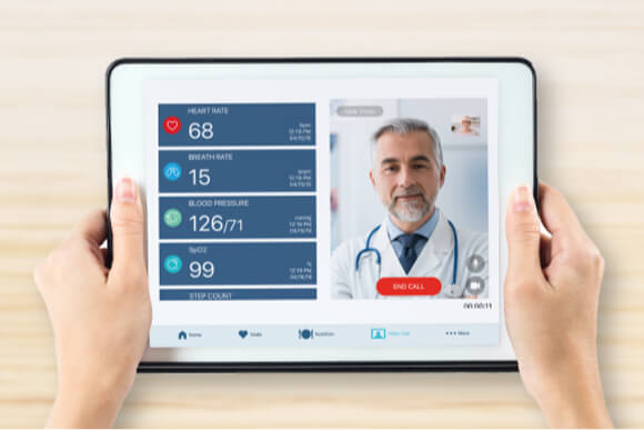 Close-up of hands holding a tablet while doctor on screen goes over patient vital signs during a telehealth appointment