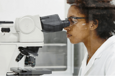 Researcher studying biofilm defense looks into a microscope in a lab