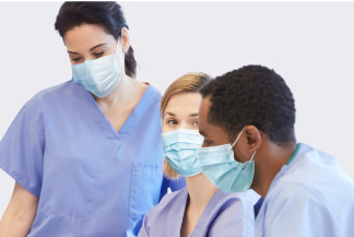  3 healthcare workers in scrubs and masks conversing with one another