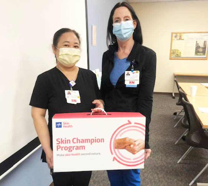 BAN_Desert Springs_Education_RGB Two Desert Springs Skin Champion team members holding up the Skin Champion program box