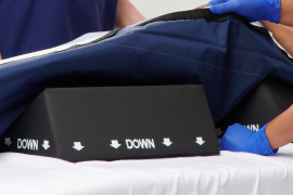 Gloved caregiver hands dispense ISP protectant cream to elderly patient’s back as they lie face down.