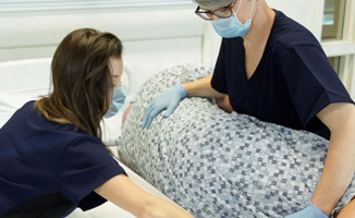 Two clinicians repositioning a patient in bed