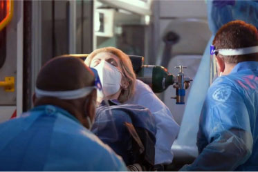 Two emergency medical services workers caring for a patient, eyes closed, laying on a gurney, wearing a mask.