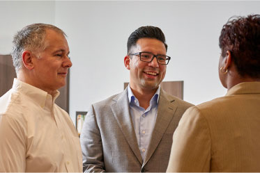 hands-on-support Three people standing and conversing, one in glasses, smiling broadly.