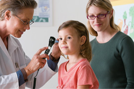 A female clinician examines a child’s ear with device while the mom observes.