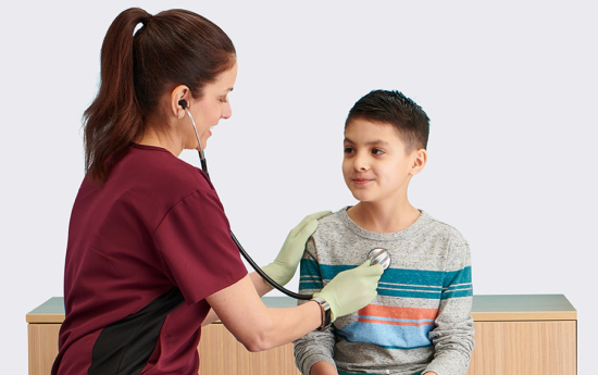 A female clinician uses a stethoscope on a boy coming to visit the physician office.