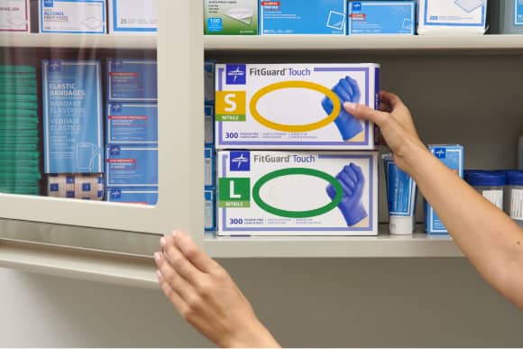 Hands reach for boxes of gloves sit on a physician office upply shelf.