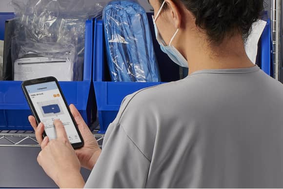 A physician office staff member uses a smartphone to inventory medical supplies.