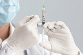 A gloved hand preps a syringe for a shot.