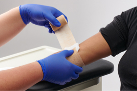 Gloved hands gauze to secure a cotton pad on a child’s arm.