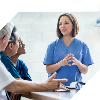 Female clinician teaches a small group of students around a table.