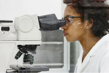 Biofilm expert looks into microscope to view pathogens in a lab Biofilm expert