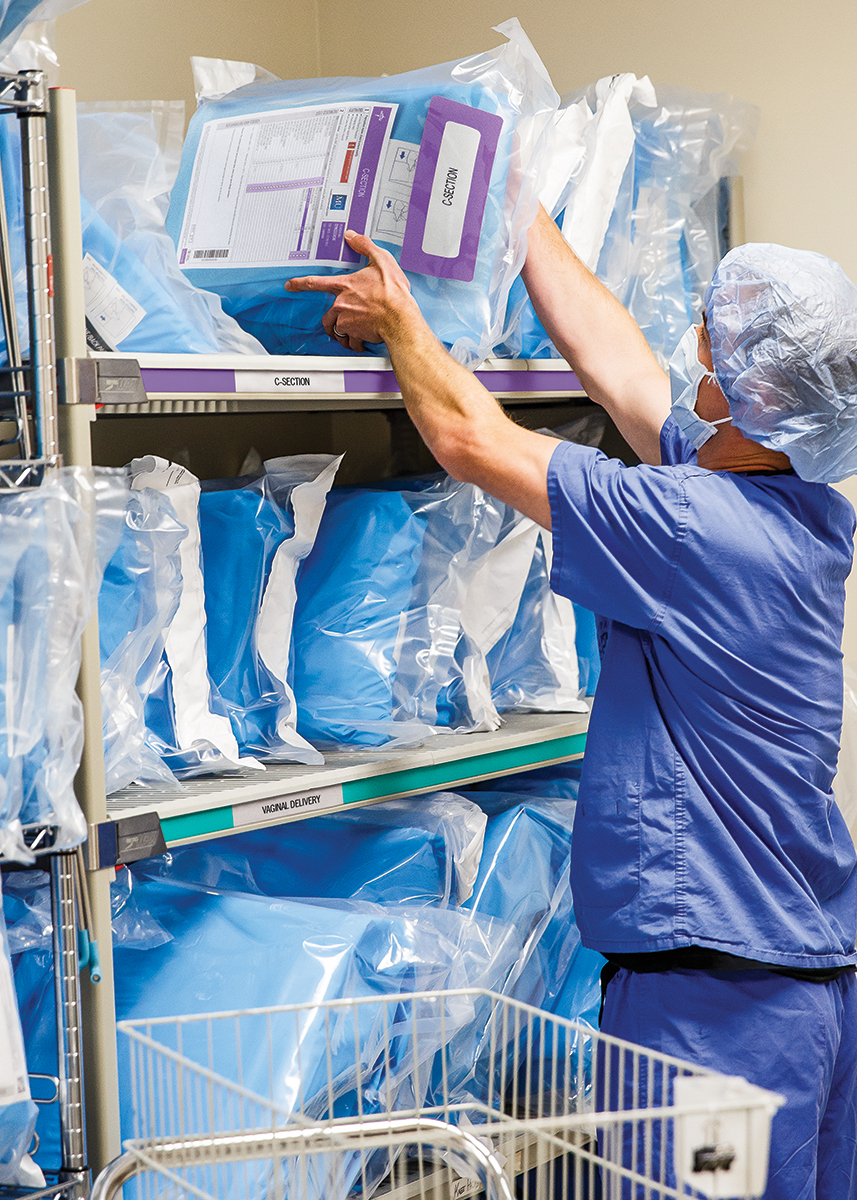 FAC_2015 Medline Stu_6084_01 copy Clinician in scrub pulls surgical pack off the shelf in an OR supply room