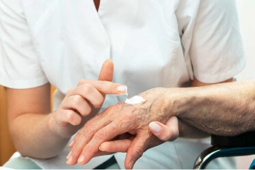 Caregiver applies cream to elderly resident’s hand as they’re seated in a wheelchair