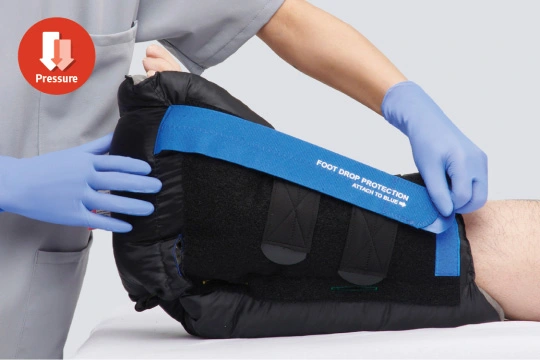 Caregiver pulls a strap on a heel positioning boot to secure it on a patient’s foot