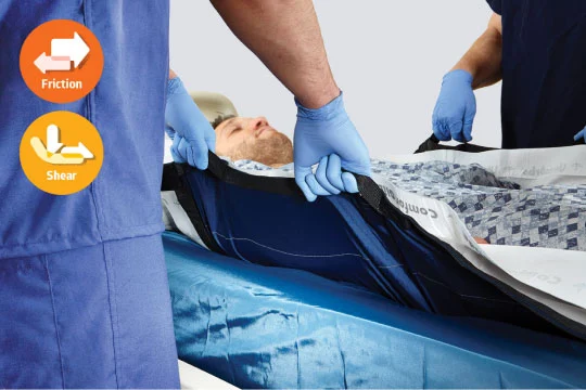 Two caregivers hold the straps on a repositioning sheet while preparing to move a patient