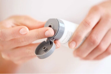 Hands prepare to squeeze product out of a tube.