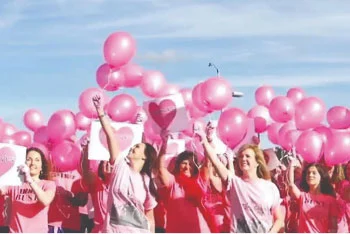 Group of women dressed in pink outside holding pink balloons.