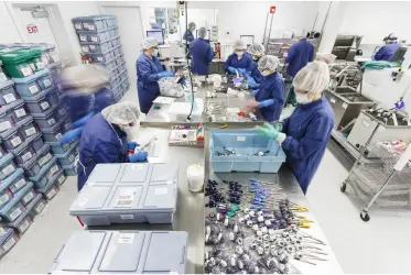 Image of people in blue scrubs and protective gear working together in a lab