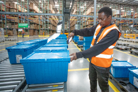 tote_exchange Man wearing orange vest in warehouse using a smartphone to scan a blue reusable bin.